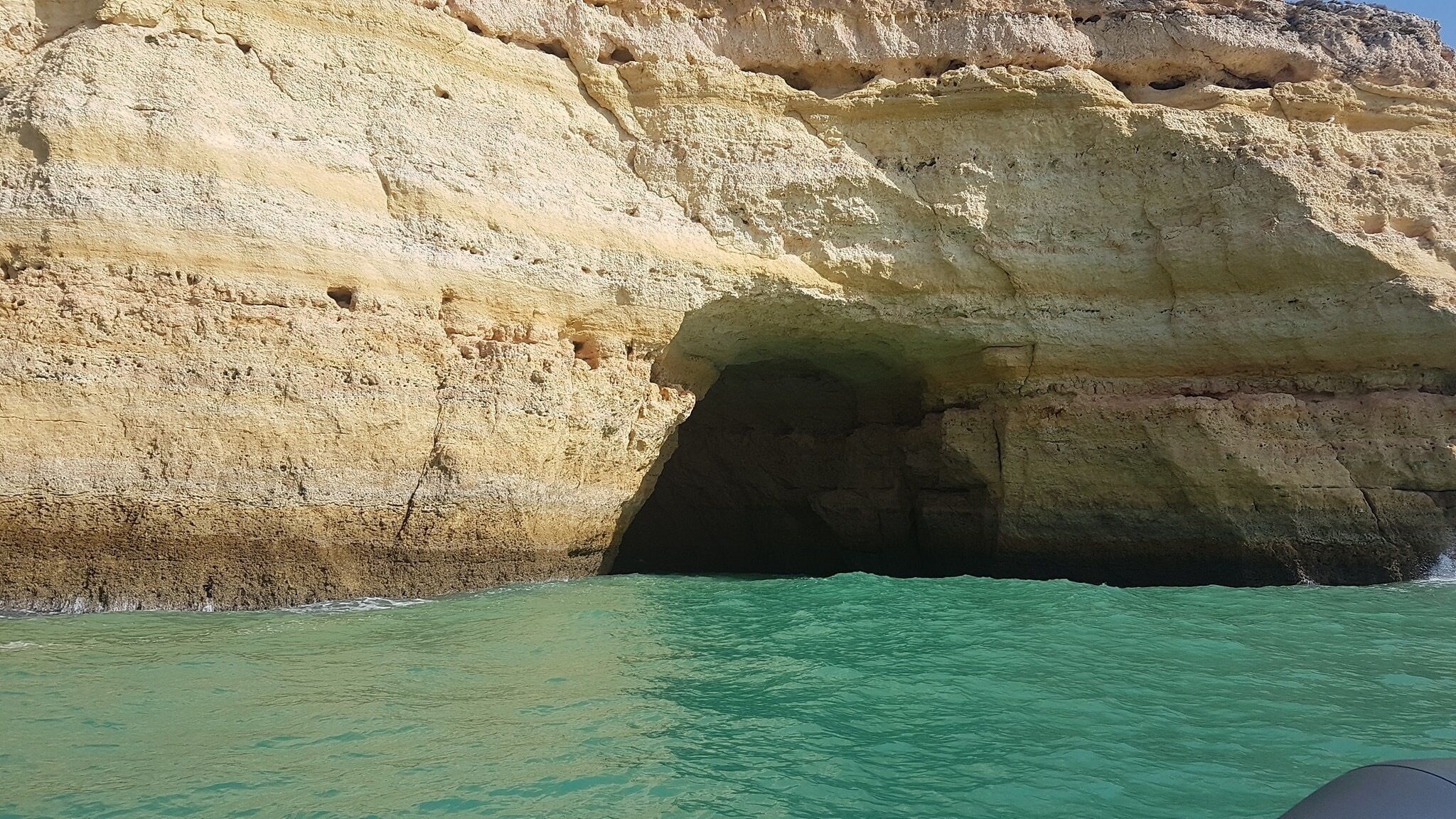 Een natuurlijke rotsformatie met een grotopening en helder turquoise water.