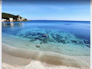 A coastal beach with clear water revealing underwater rocks, a sandy shore, and buildings on a hillside in the background. - Luxury villa with private pool 500m from the beach St Cyprien Porto Vecchio (Lecci)