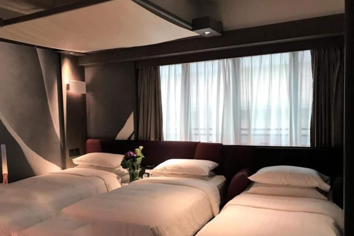 A hotel room with two beds, a large window with curtains, and a modern ceiling design.