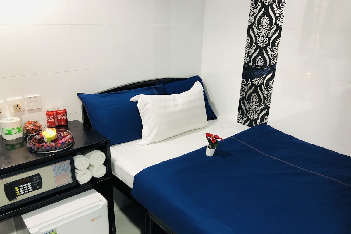 A hotel room with a bed, a bedside table with a lamp, a small plant, and a minibar.