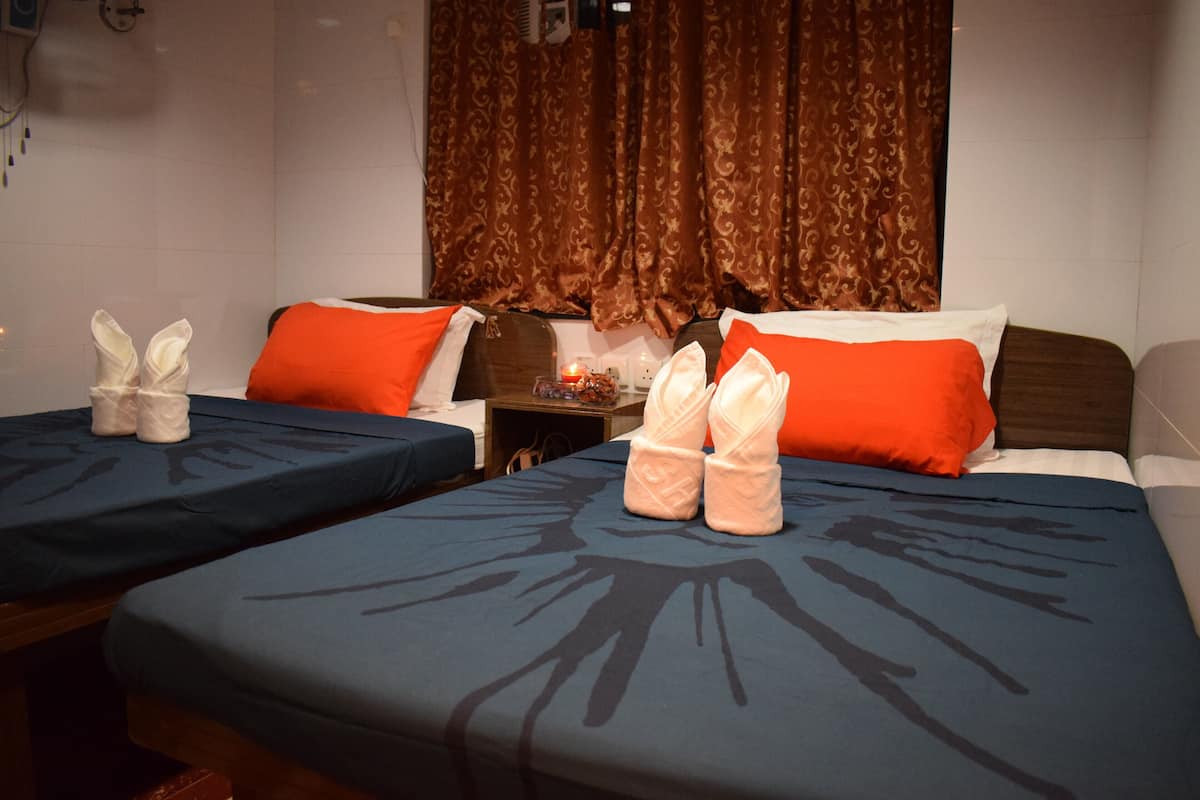 A hotel room with two beds, each with a blue bedspread and orange pillows. There are towels placed on the beds.