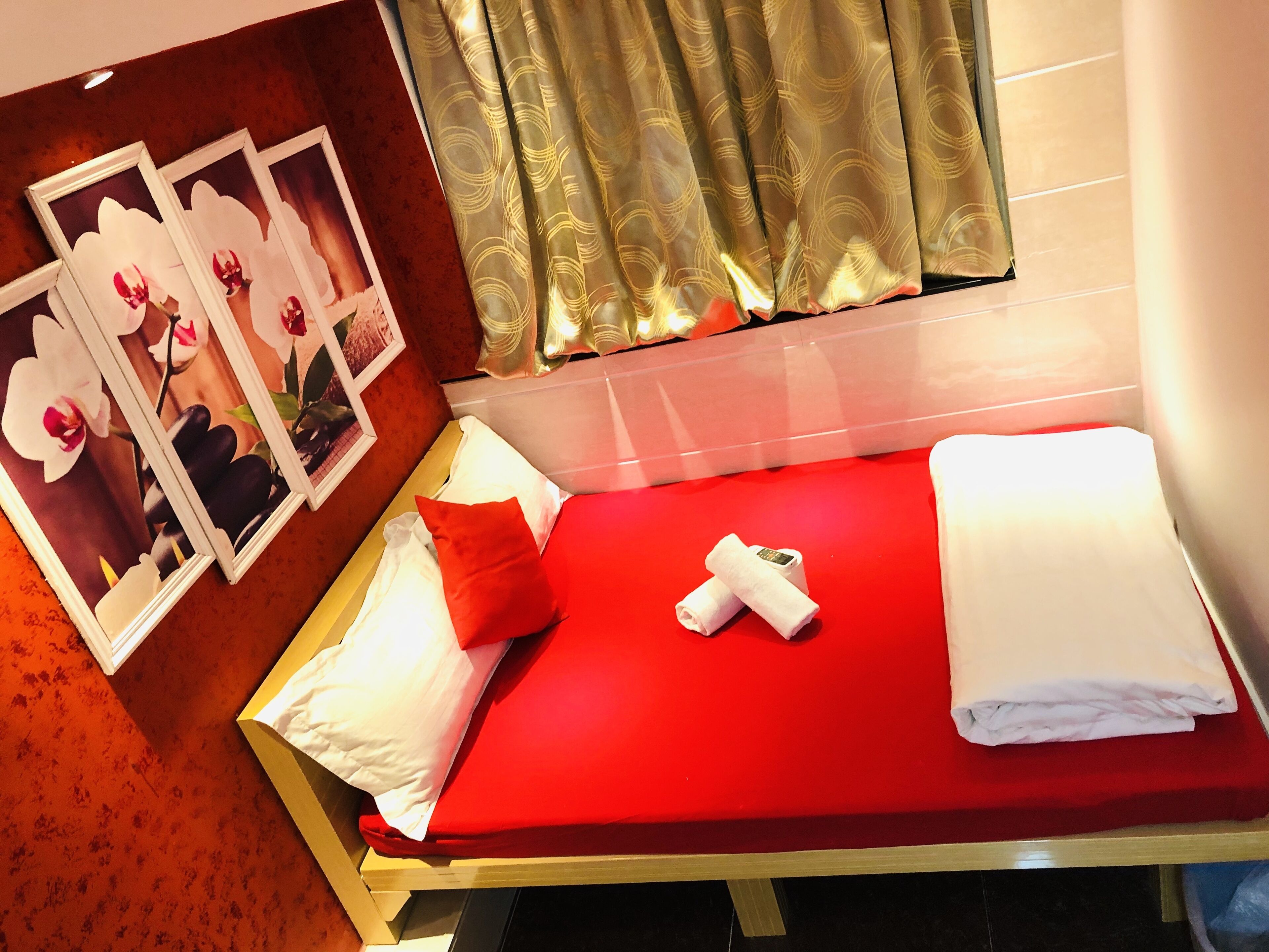 Quarto de hotel com colcha vermelha, almofadas brancas e vermelhas, uma toalha enrolada e um quadro com flores na parede.