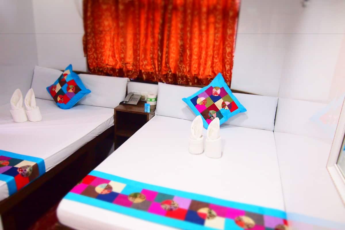 A hotel room with two beds, each with a pillow featuring a colorful quilt pattern. There are two white slippers placed on each bed.