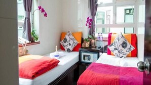 Une chambre d’hôtel avec deux lits, chacun recouvert d’une couverture rouge, une petite table avec une lampe et une fenêtre avec des rideaux.