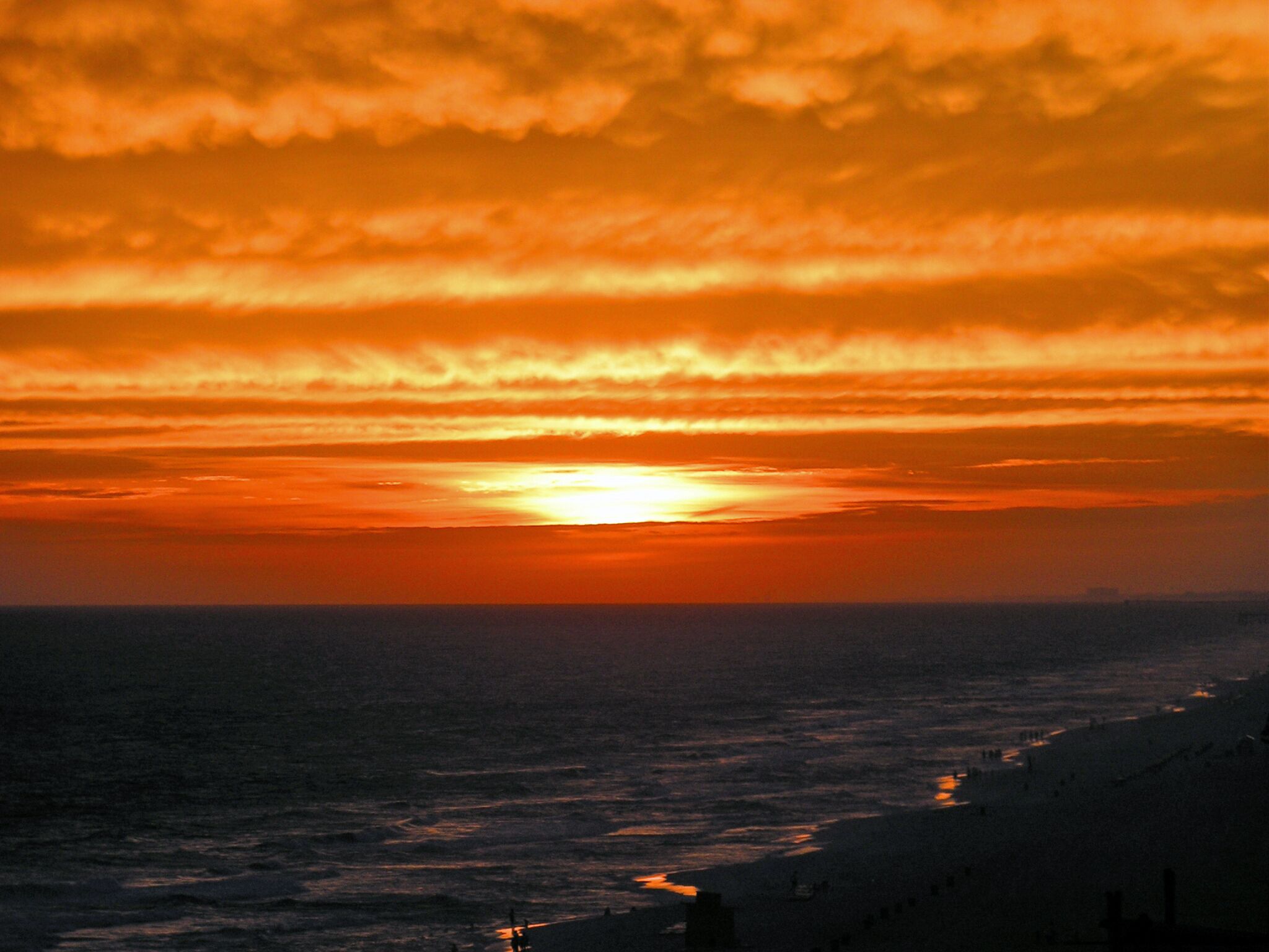 Un atardecer sobre el océano con una playa en primer plano.