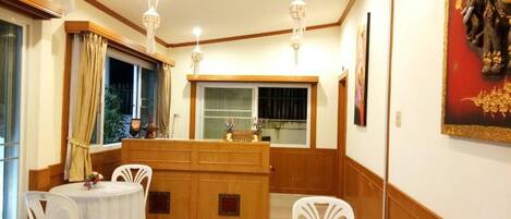 A dining area with two round tables, white chairs, a wooden counter, and pendant lighting.