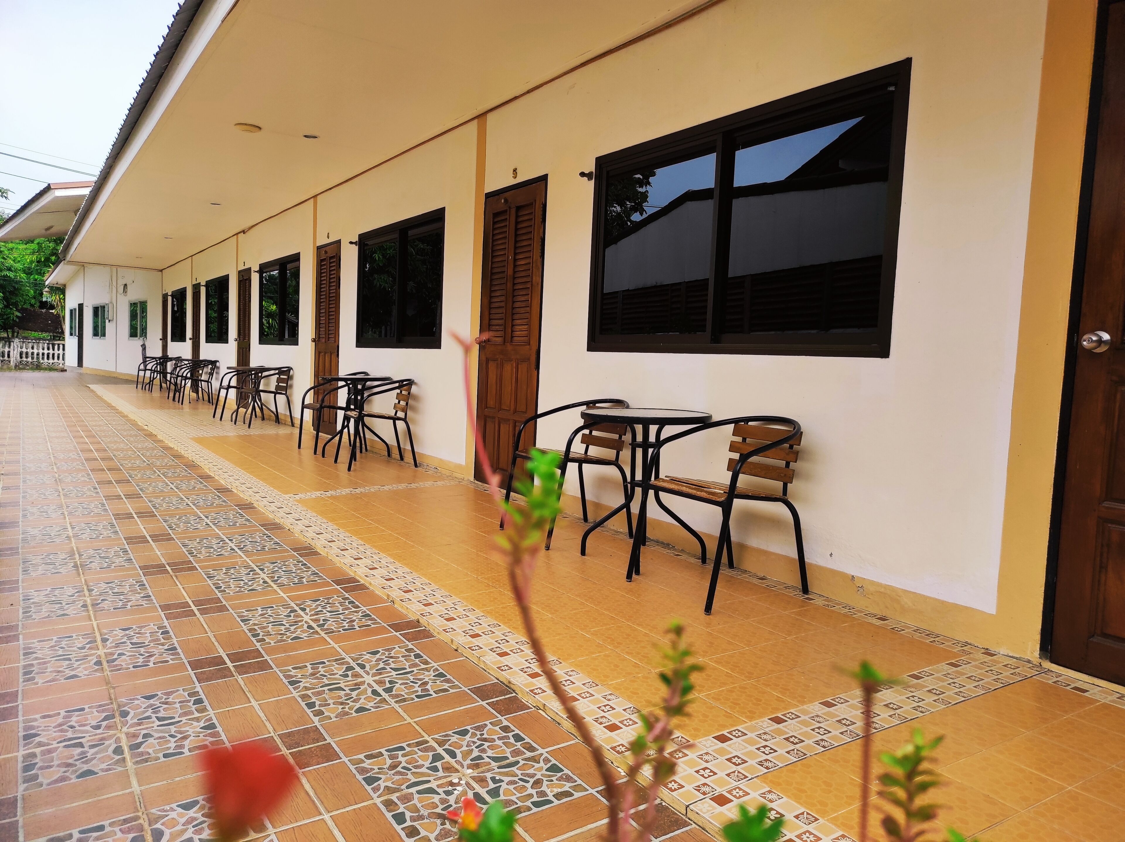 A covered outdoor seating area with tiled flooring and multiple tables and chairs.