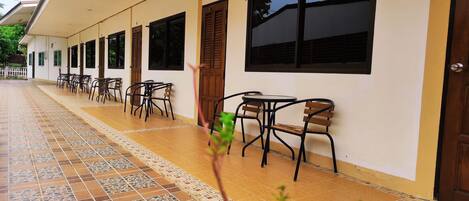 A covered outdoor seating area with tiled flooring and multiple tables and chairs.
