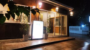 A building with a glass entrance, potted plants, and illuminated signage. - Na Soi 5 Chiangkhan (Chiang Khan)