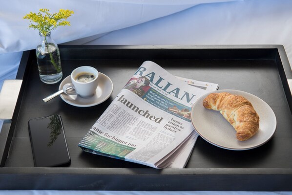 A tray with a newspaper, a croissant, a cup of coffee, a smartphone, and a small vase with flowers. - Abode Murrumbateman (Murrumbateman)