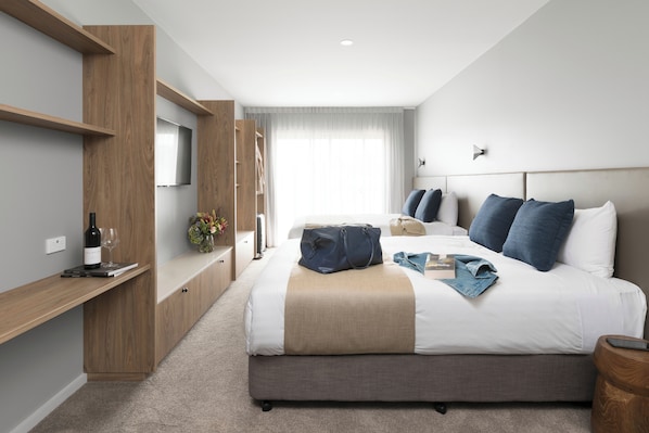 A modern hotel room with a large bed, a TV mounted on the wall, a wardrobe, and a bedside table with a wine bottle and glasses. - Abode Murrumbateman (Murrumbateman)