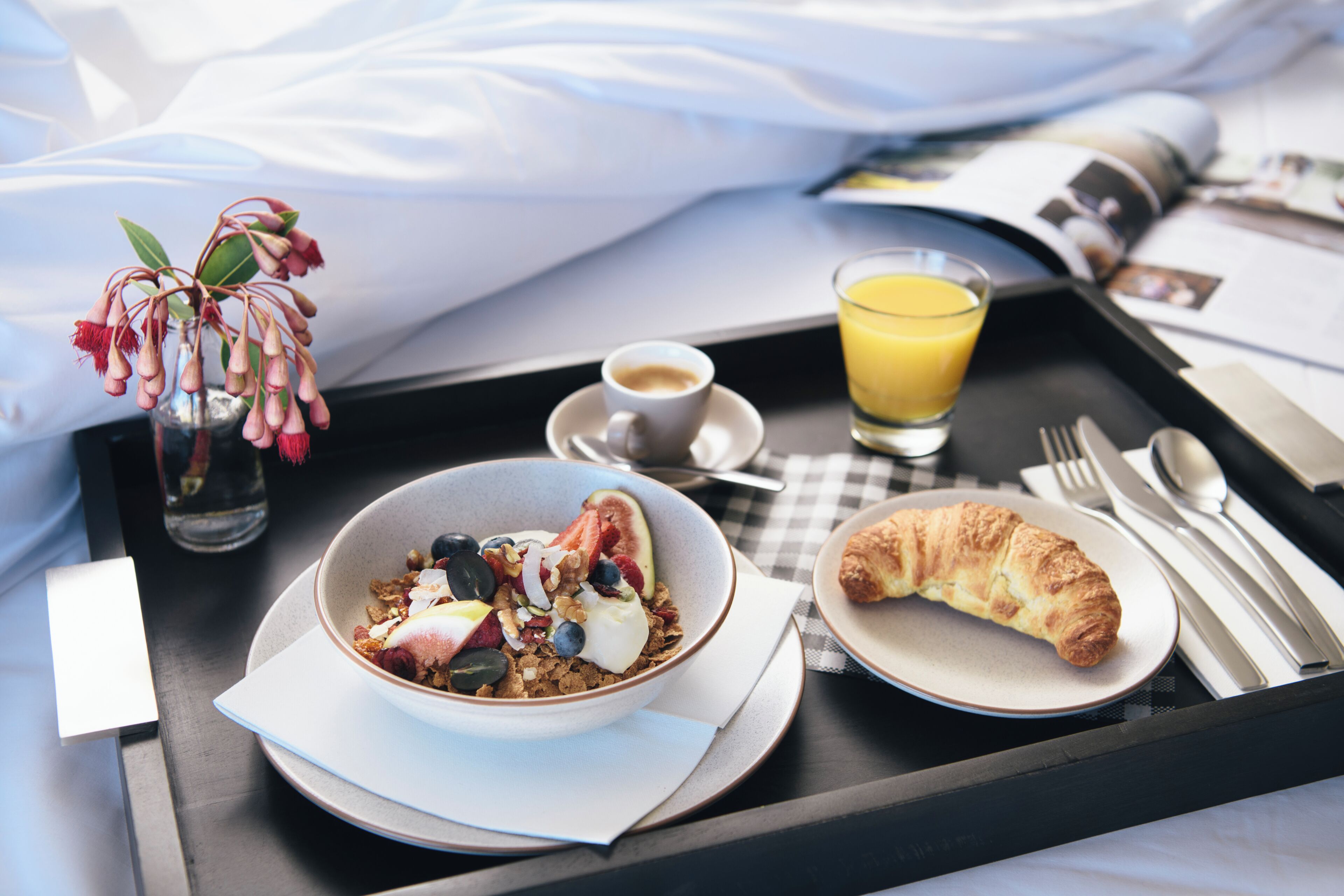A breakfast tray with a bowl of cereal, a croissant, a glass of orange juice, and a cup of coffee.