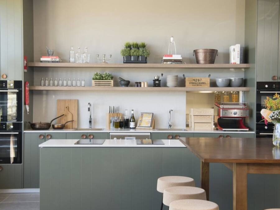 A modern kitchen with a central island, built-in appliances, and open shelving with various kitchen items.