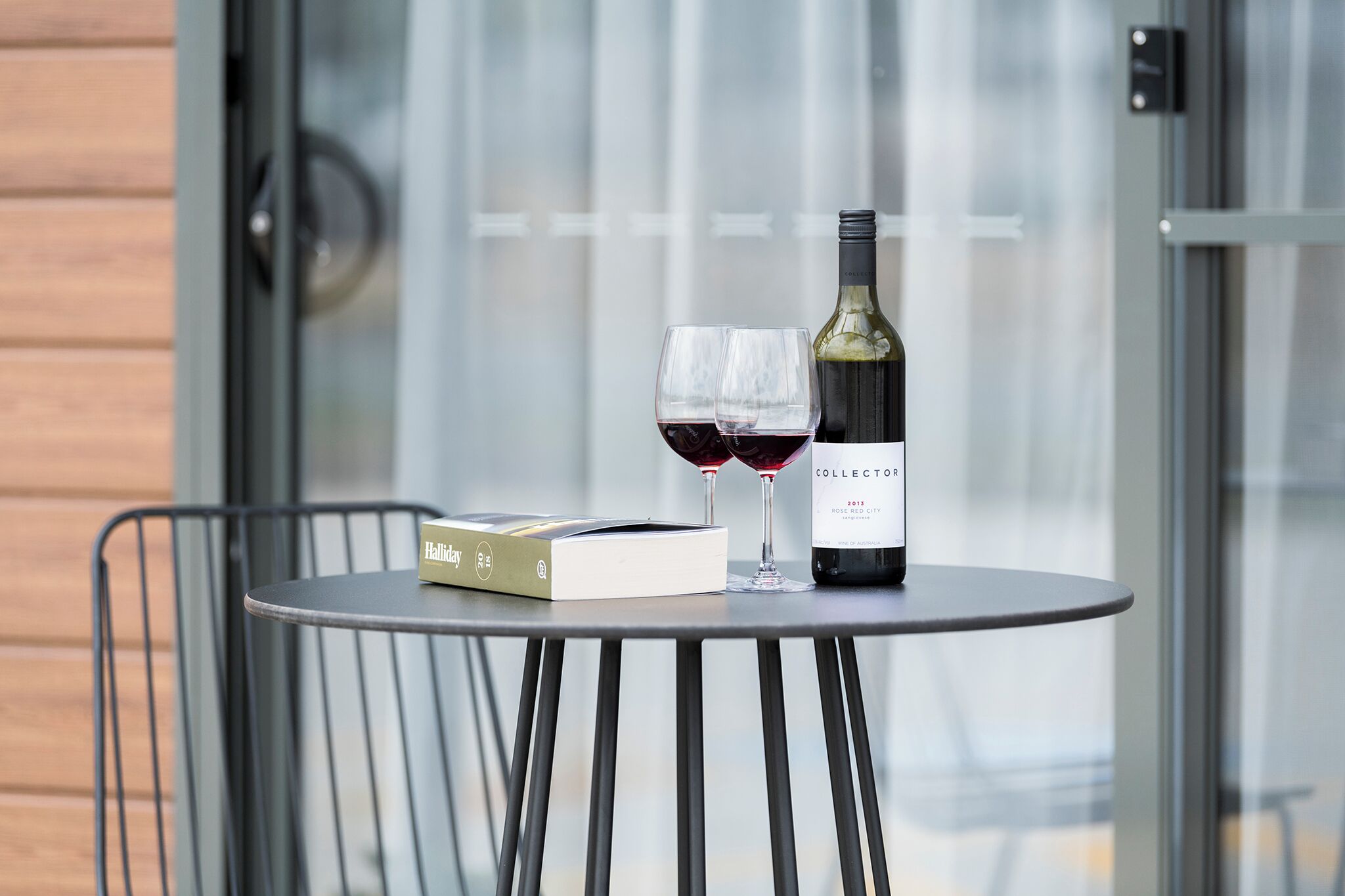 Una mesa redonda con una botella de vino, copas, un libro y una caja pequeña.