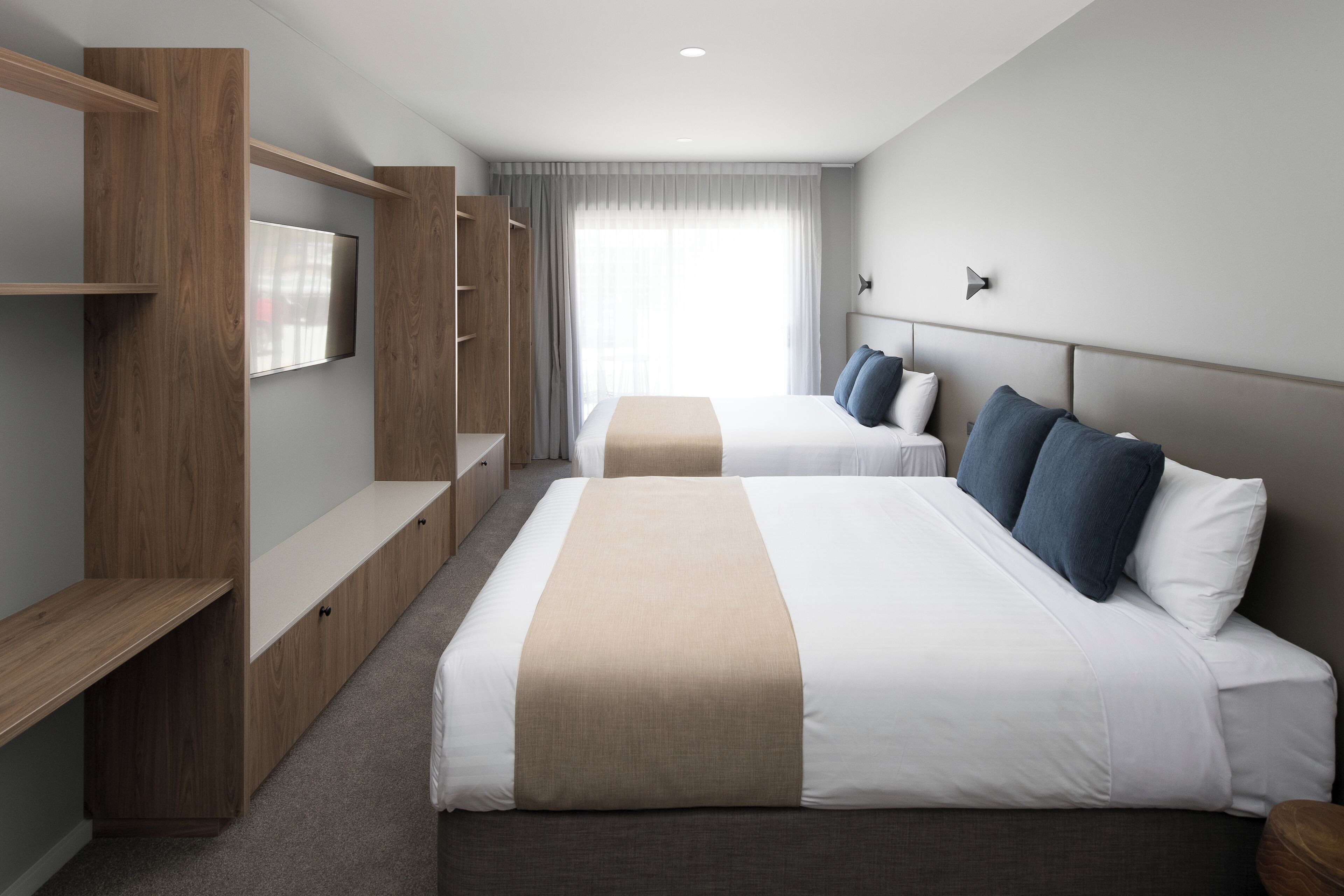 A hotel room with two beds, a TV, a wardrobe, and a large window.