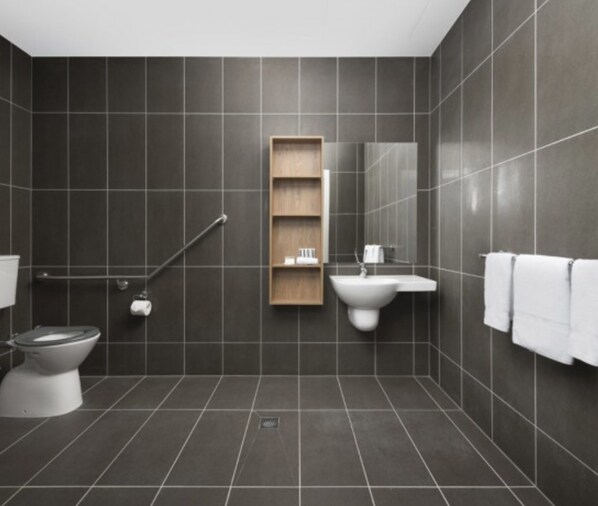 Un baño moderno con azulejos oscuros, un inodoro, un lavamanos, un espejo y una estantería de madera.