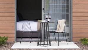 A modern room with a bed, a small table with two chairs, and a sliding glass door leading to a balcony.