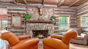 A log cabin interior with leather armchairs, a stone fireplace, and a deer head mounted on the wall. - TWO Amazing Log Cabins, Storybook Setting, Hot Tub, WiFi, Mountain Views Pets Ok (Gerton)
