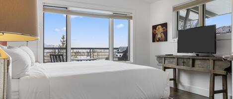 Ein Schlafzimmer mit einem großen Bett, einem Fernseher, einem Schreibtisch und einem Fenster mit Blick ins Freie.