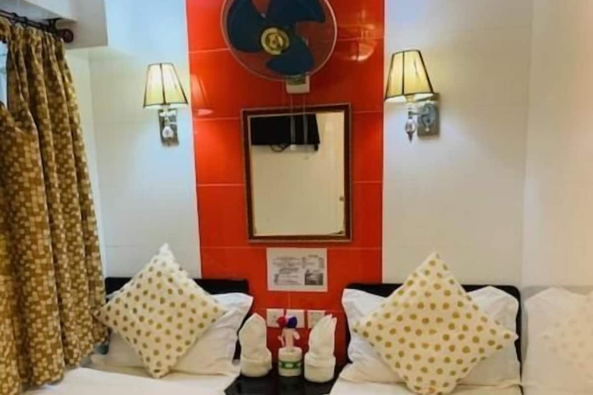 A hotel room with two single beds, a red wall, a ceiling fan, and two wall-mounted lamps.