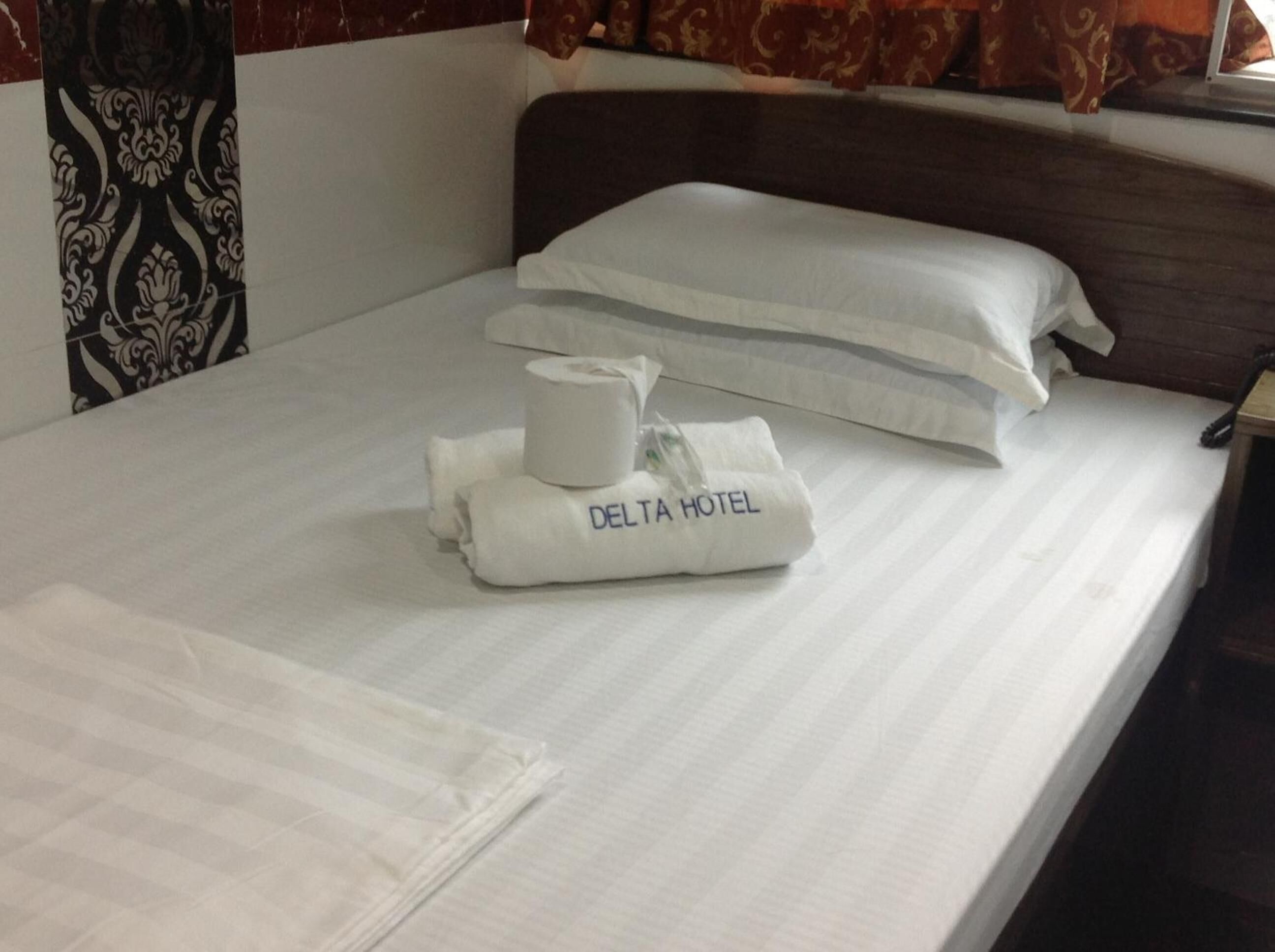 A neatly made bed with white linens, a pillow, a rolled towel, and a small bag labeled "DELTA HOTEL" on a hotel room.