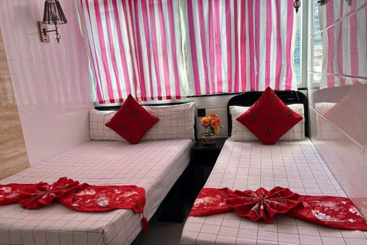 A hotel room with two beds, each with a red decorative pillow and a red floral bedspread.