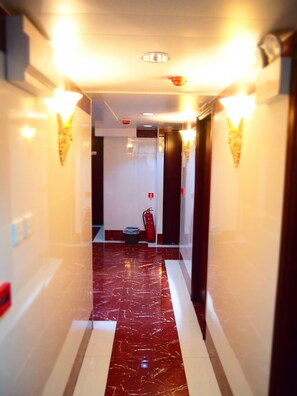 Ein Hotelgang mit Marmorboden, Wandleuchten, einem Feuerlöscher und einem Mülleimer.