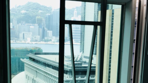 A view from a window of a building with a modern glass facade, a large cylindrical structure in the background, and a street with a bus stop. - Premium Lounge (Kowloon)