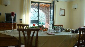 Un coin repas avec une table dressée pour deux personnes, un téléviseur posé sur un meuble en bois et une vue par la fenêtre, qui est ornée de rideaux.