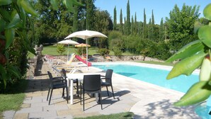 Un espace piscine équipé d’un toboggan, de parasols et de mobilier d’extérieur.