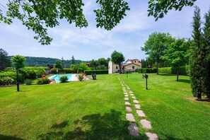 A well-maintained garden with a swimming pool, stone pathway, and a building with a tiled roof.