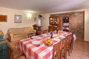 A dining area with a table set for four, surrounded by wooden chairs, a wooden cabinet, and a stone wall.