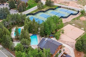 Luchtbeeld van een woongebied met een tennisbaan, een zwembad en een huis omringd door bomen.
