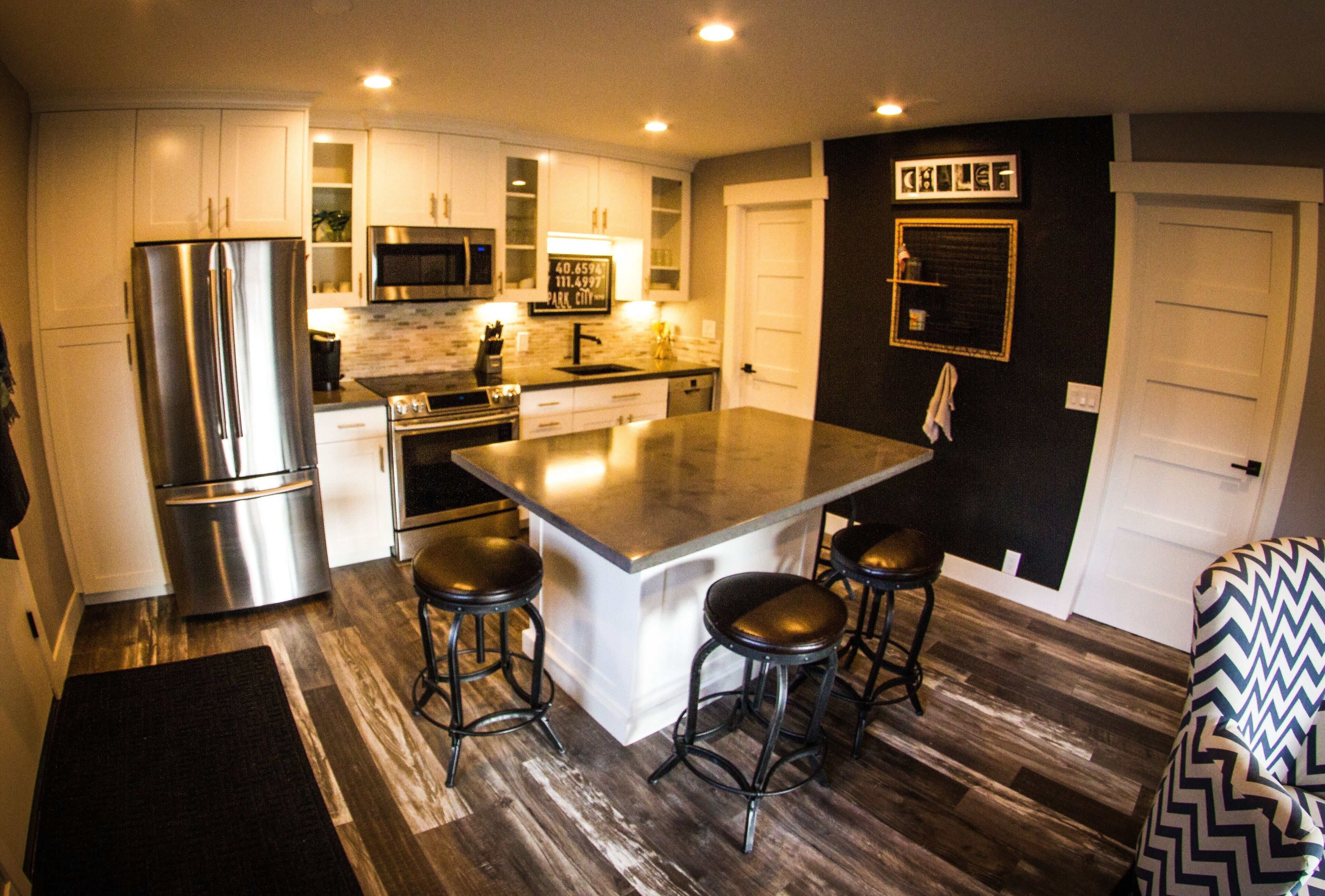 Una cocina moderna con electrodomésticos de acero inoxidable, una isla central con taburetes y un sofá con estampado blanco y negro.