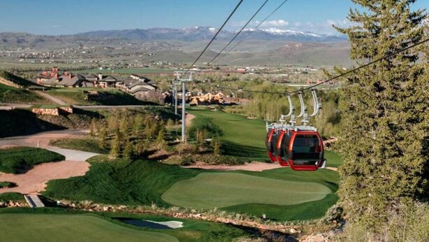 Un sistema de teleférico sobre un campo de golf con montañas al fondo.