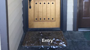 Una porta di legno con una serratura di sicurezza in metallo, uno spioncino e una cassetta postale, con uno zerbino coperto di neve.