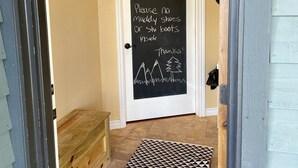 Una porta con un cartello alla lavagna che dice “BENVENUTI a WP! Si prega di non portare scarpe fangose o scarponi da sci all’interno. Grazie!” con un disegno di montagna e albero.