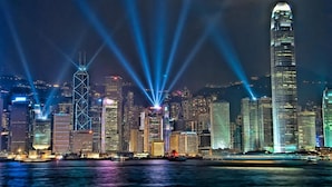 A nighttime cityscape with illuminated skyscrapers and a river in the foreground. - Traveller's Hostel (Kowloon)