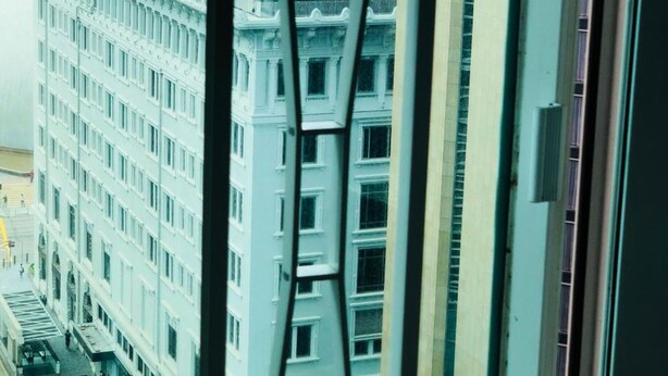 A view from a high-rise window overlooking a cityscape with modern buildings and a waterfront. - Traveller's Hostel (Kowloon)