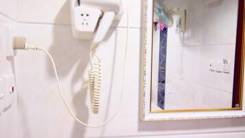 A bathroom with a white wall, a hairdryer, a power outlet, and a mirror with a gold frame.
