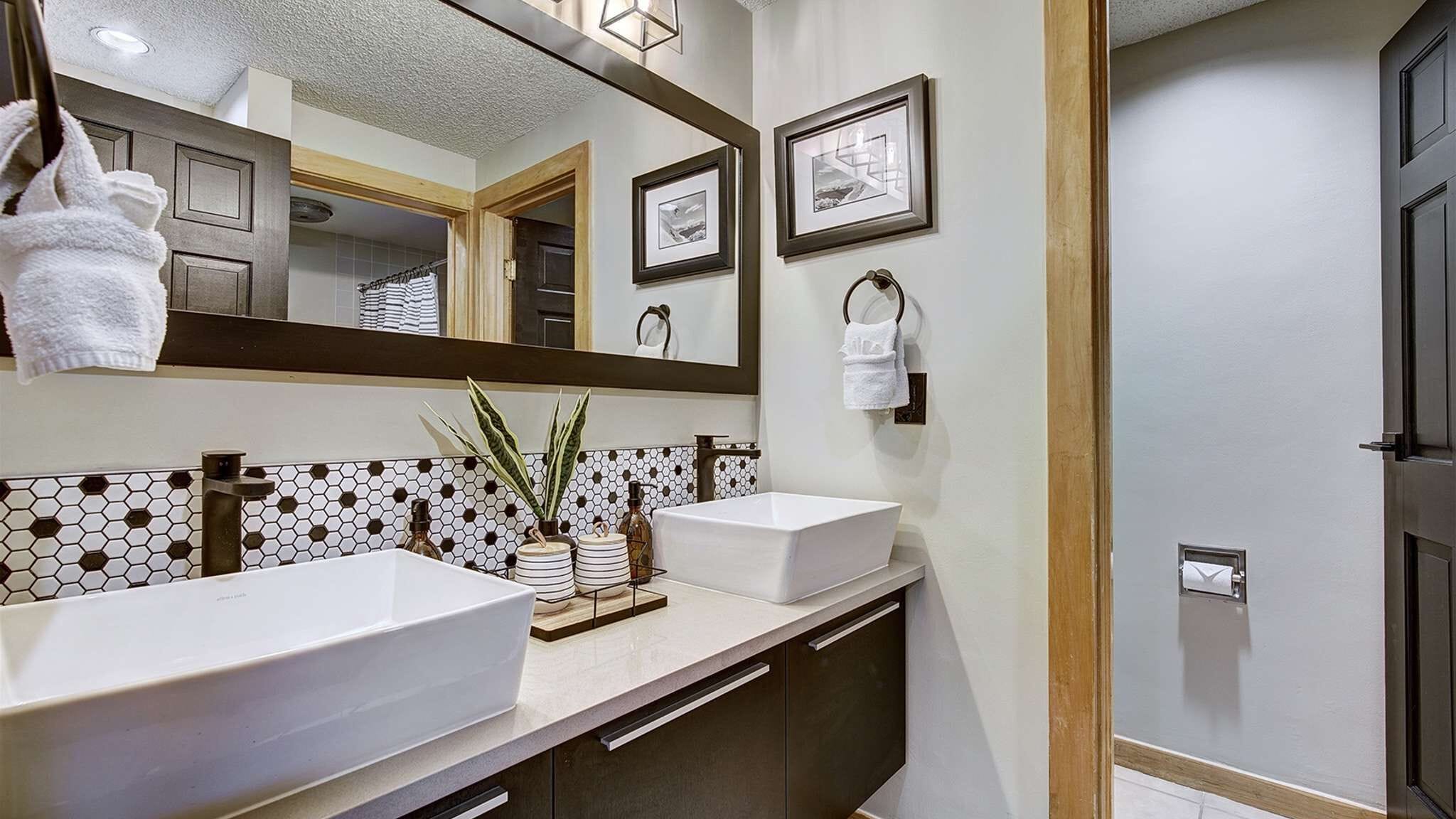 A bathroom with two sinks, a large mirror, and a tiled backsplash.