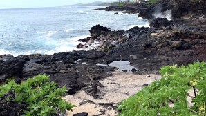 A rocky shoreline with ocean waves crashing against the rocks, green vegetation in the foreground, and a clear view of the sea. - STUNNING OCEANFRONT * Poipu's Best View * New Air Conditioning throughout (koloa)