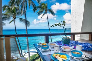 A balcony with a table set for breakfast, overlooking a tropical beach with palm trees and the ocean. - STUNNING OCEANFRONT * Poipu's Best View * New Air Conditioning throughout (koloa)