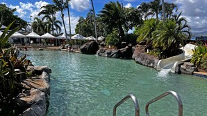 A pool with a slide, surrounded by rocks and palm trees. - STUNNING OCEANFRONT * Poipu's Best View * New Air Conditioning throughout (koloa)