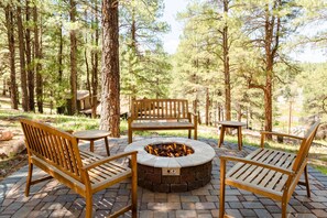A circular fire pit surrounded by wooden benches and tables in a forested area. - The Private Toho-Tel Suite (Flagstaff)