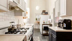 A modern kitchen with white cabinets, a gas stove, a kettle, and a coffee maker.