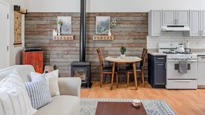 A cozy living room with a fireplace, dining table, and kitchen area with white cabinets and a stove.