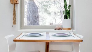 A dining area with a table set for two, a macrame plant hanger, and a potted plant by the window.
