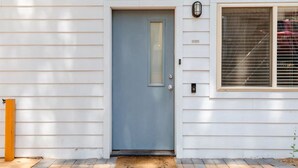 A house with a blue front door, a small window with blinds, and a wooden post to the left.