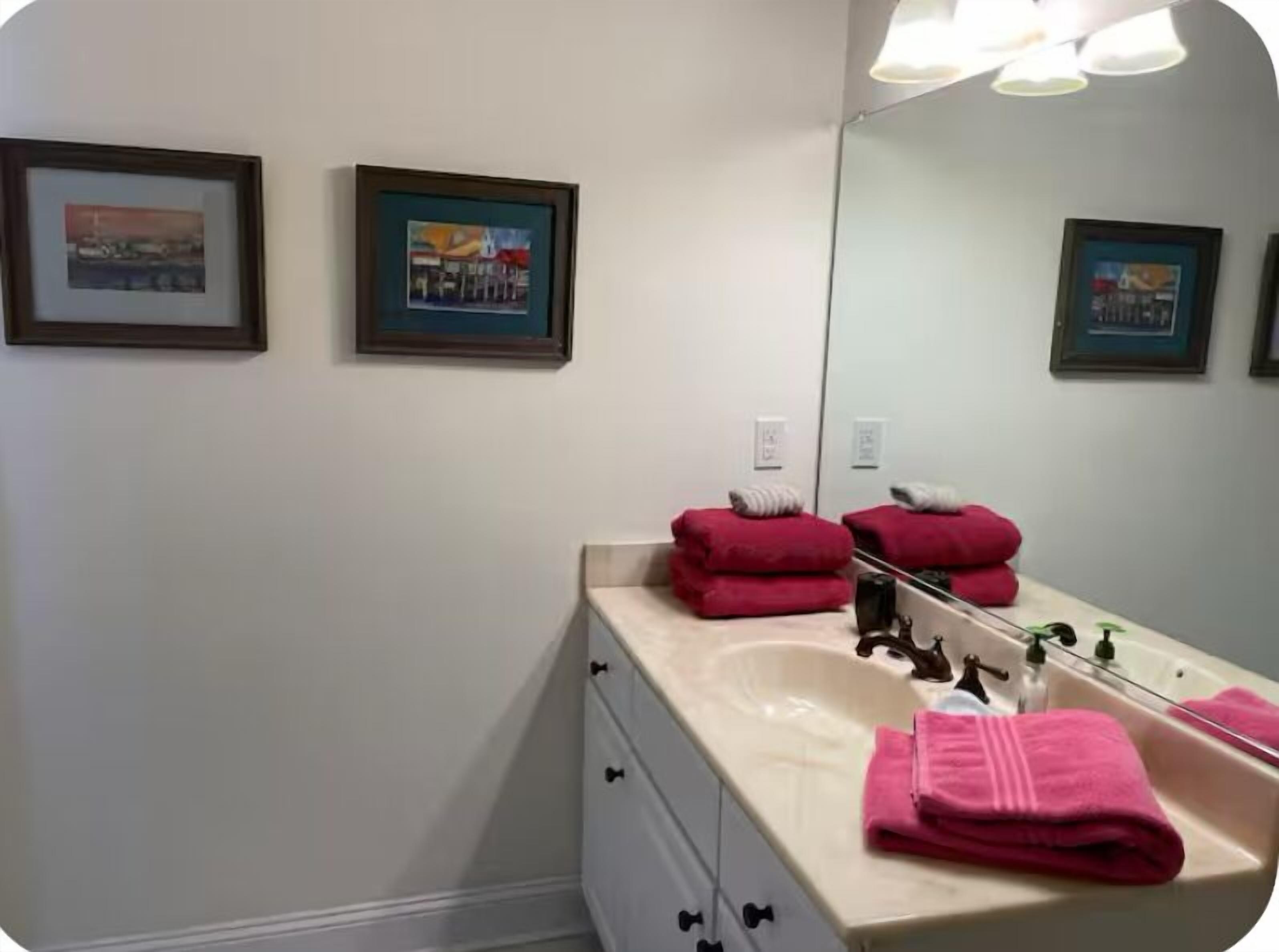 A bathroom with a sink, mirror, and two framed pictures on the wall.